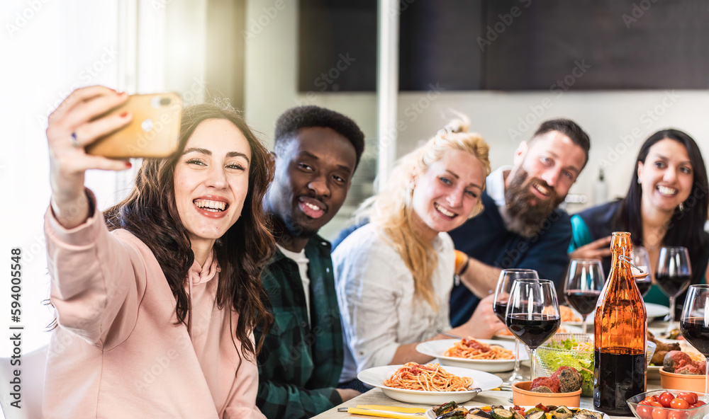 Multiethnic guys and women taking selfie for lunch in the home kitchen - Young friends having fun together in the apartment while eating delicious italian spaghetti with tomato sauce - Bright filter