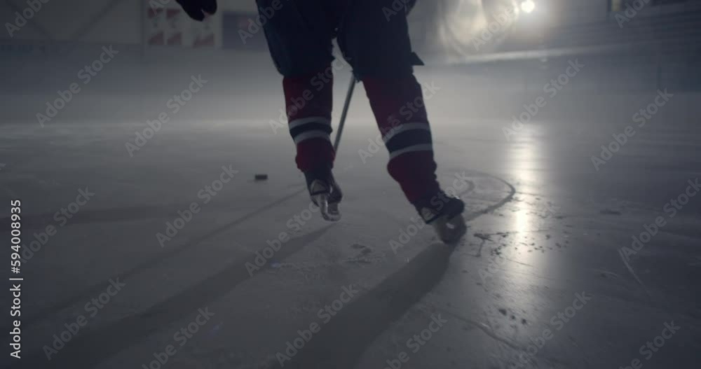 Hockey player in red uniform skating on ice stick handling puck in the dark
