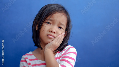 Asian kid girl toothache. Kid suffering from toothache. Asian child hand on cheek face as suffering from facial pain, mumps toothache. Dental health care.