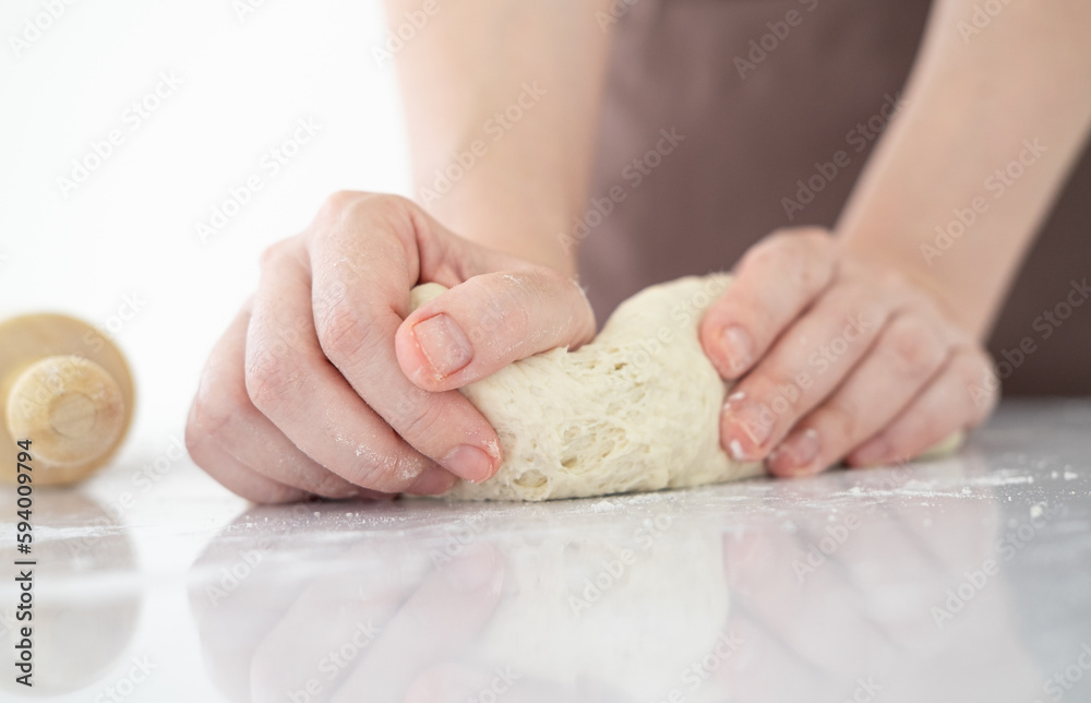 Close up of  home baker chef is making with flour loaf of dough for preparation of pasta, pizza and other pastries in bright bakery kitchen.Female hands making dough for pizza .