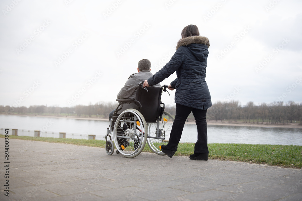 A woman pushes a disabled person in a wheelchair.