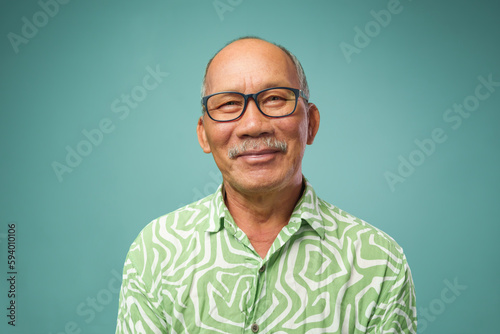 Portrait of Asian senior adult man in green T-shirt and eyeglasses smiling looking at camera indoors. Middle aged old senior confident over isolated background.