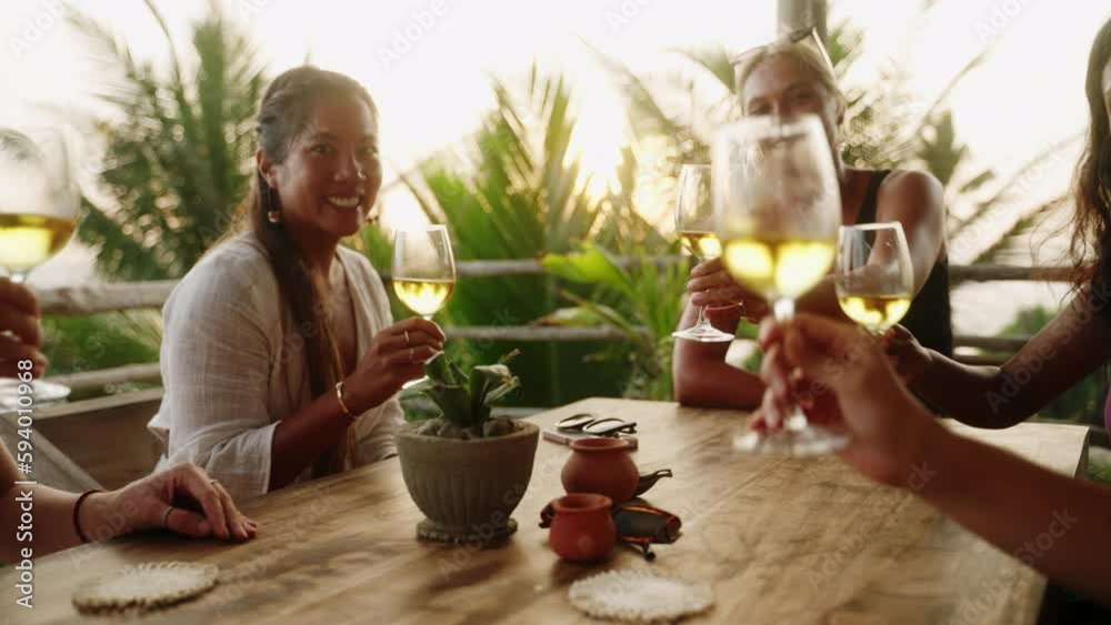 Multiracial women cheering and clinking glasses with wine enjoying dinner party in outdoor sea view cafe. Young multiethnic female friends drinking alcohol, having fun in tropical rooftop restaurant Multiracial women cheering and clinking glasses with wine enjoying dinner party in outdoor sea view cafe. Young multiethnic female friends drinking alcohol, having fun in tropical rooftop restaurant