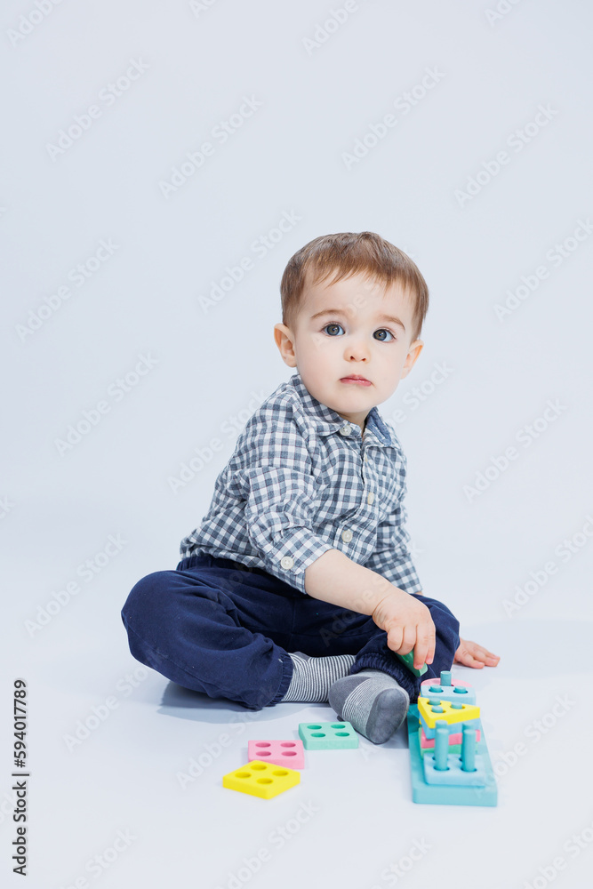 A cute little boy in a checkered shirt sits on a white background and plays with wooden educational toys. Ecological wooden toys for children A cute little boy in a checkered shirt sits on a white background and plays with wooden educational toys. Ecological wooden toys for children