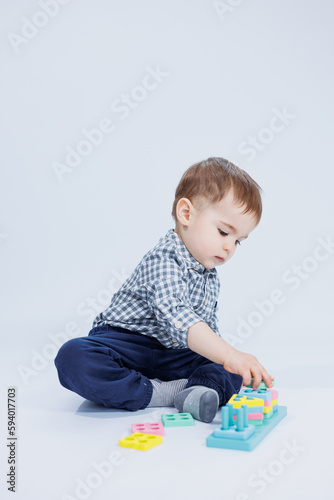 A cute little boy in a checkered shirt sits on a white background and plays with wooden educational toys. Ecological wooden toys for children