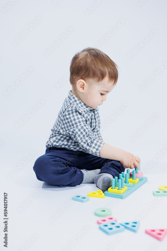 A cute little boy in a checkered shirt sits on a white background and plays with wooden educational toys. Ecological wooden toys for children A cute little boy in a checkered shirt sits on a white background and plays with wooden educational toys. Ecological wooden toys for children