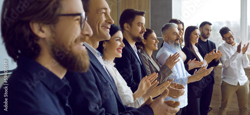 Audience applauding speaker after successful presentation at business conference or office meeting. Team of happy people standing in row, smiling and clapping hands all together. Side, profile view