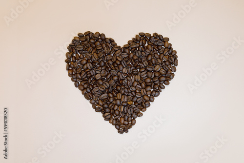 Coffee beans in heart shape on pink peach background.