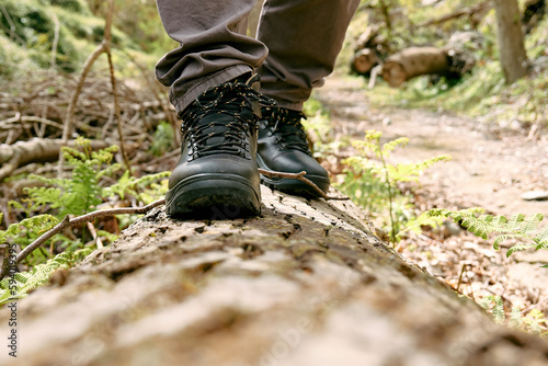 Fototapeta Naklejka Na Ścianę i Meble -  Traveler man has hiking in mountain forest. Close up of human foots in mountain shoe walking on tree log. Exercise and fitness in nature for wellness and healthy lifestyle.