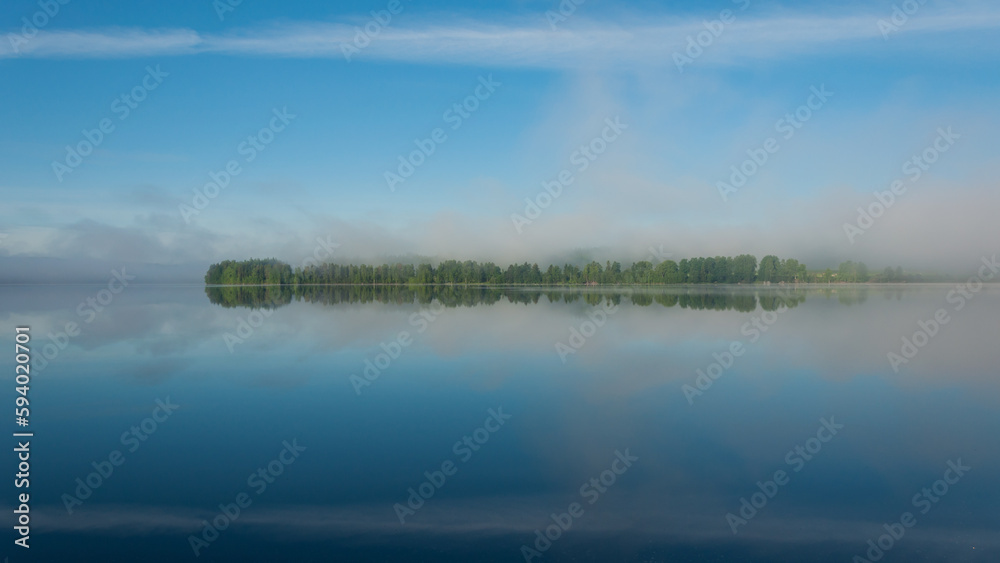 Summer lake scenery with clouds and mist reflected on the water in Finland