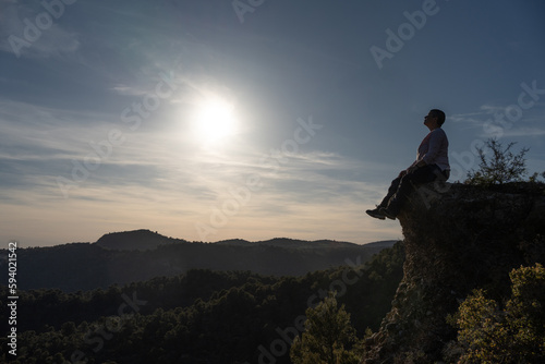 Landscape with a large horizon at sunset  on the top of a rock at the top a non-binary woman reflecting and thinking about life and the paths to follow.