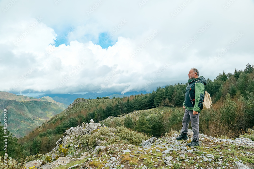 Traveler man hiking in mountain forest, standing on the stone and looking on panoramic mountain valley.