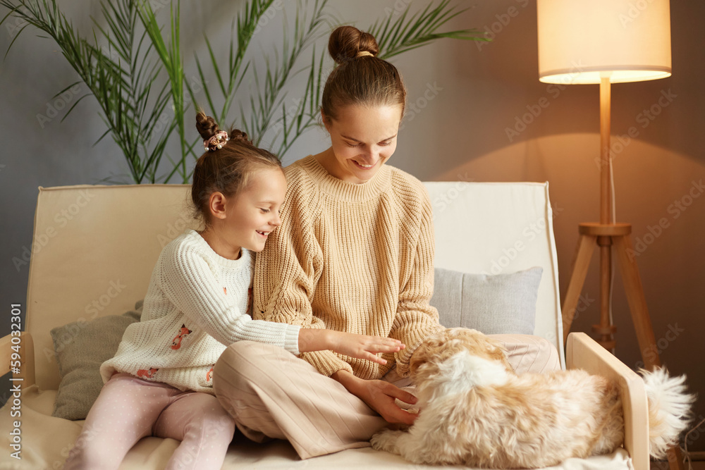 Happy delighted family spending time at home sitting on sofa playing with dog leisure time with favorite pat posing in home interior smiling happily. Happy delighted family spending time at home sitting on sofa playing with dog leisure time with favorite pat posing in home interior smiling happily.