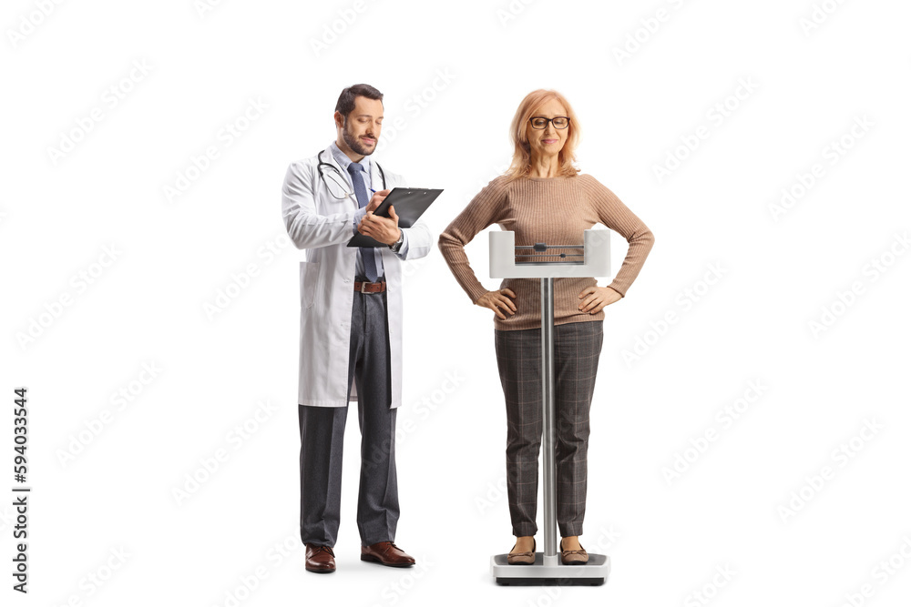 Mature woman weighing on a scale gesturing happiness and a male doctor writing a document Mature woman weighing on a scale gesturing happiness and a male doctor writing a document