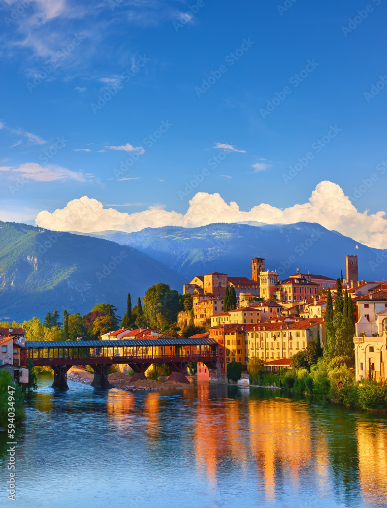 Bridge Ponte Degli Alpini at River Brenta Bassano Del Grappa Italy. Panoramic View Old Town with Vintage Building and Tower Wooden Background Alpine Mountains Scenic Landscape Evening Sunset