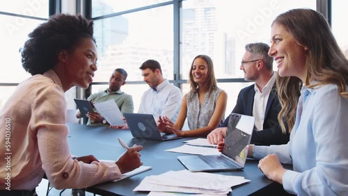 Multi-cultural business team meeting around office boardroom table with laptops discussing documents - shot in slow motion