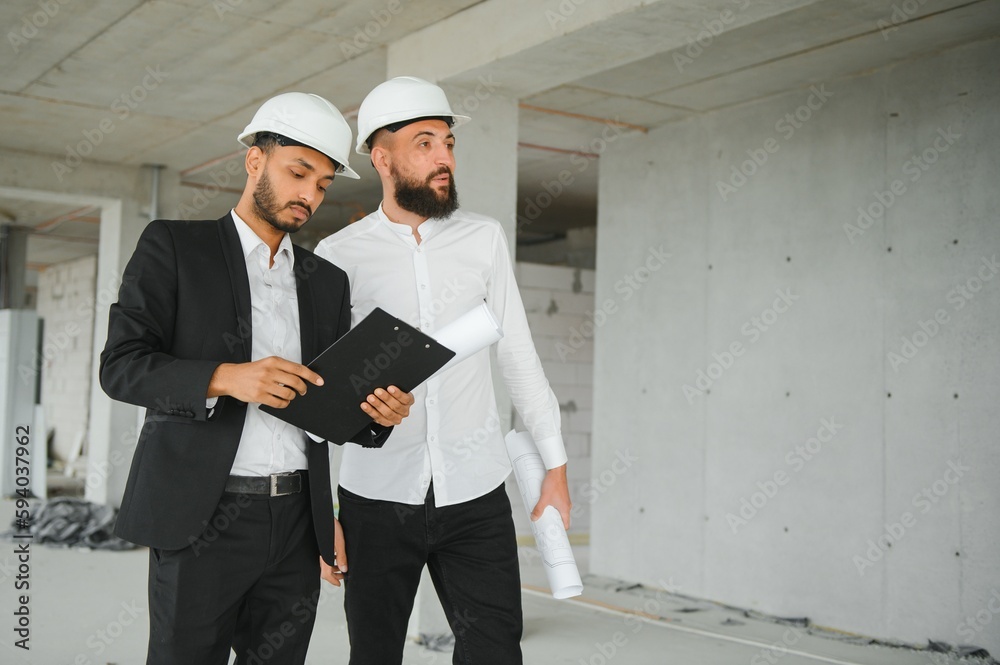 Multiracial male coworkers in hardhats discussing project on construction site Multiracial male coworkers in hardhats discussing project on construction site