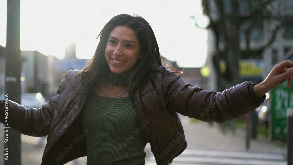 One happy young woman dancing in street celebrating during sunset time. A joyful 20s adult girl walking while she dances feeling carefree