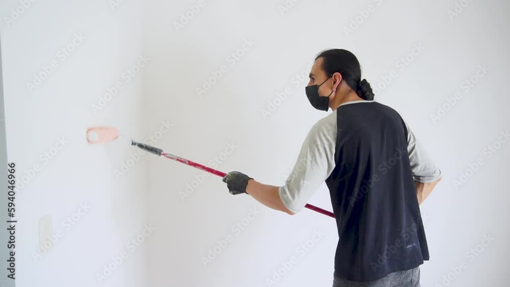 Latin American man painting a wall, skillfully applying paint as part of a temporary job or home renovation project. non-agricultural work visa for seasonal jobs Latin American man painting a wall, skillfully applying paint as part of a temporary job or home renovation project. non-agricultural work visa for seasonal jobs