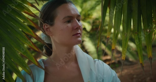 Young woman enjoying nature under palm tree leaves in tropical forest park. Unity with nature. Earth day. photo
