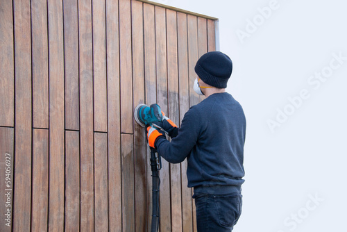 Professional renovation of hardwood cladding, man sanding, removing oxidation and dirt cleaning wood siding with an orbital power sander, empty copy space photo