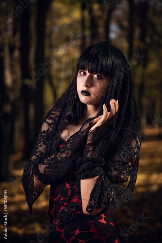 Vertical shot of a mysterious gothic girl with dark witch clothes looking at the camera