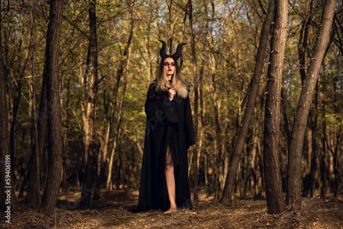 Gothic young girl with the Maleficent horns and a black cape  in forest