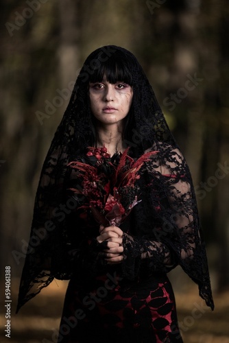 Vertical portrait of a scary corpse bride holding red flowers in the autumn forest