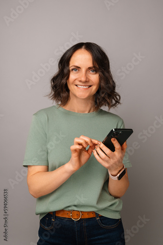 Vertical shot of a woman using a smart phone while smiling at the camera.