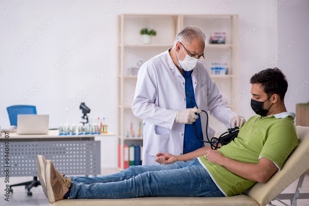 Old male doctor measuring young patient's blood pressure Old male doctor measuring young patient's blood pressure