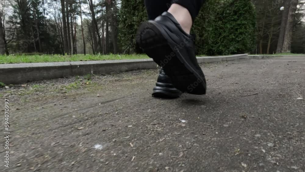 Female feet in black sneakers walk along the paths and sidewalks of city streets and parks Female feet in black sneakers walk along the paths and sidewalks of city streets and parks