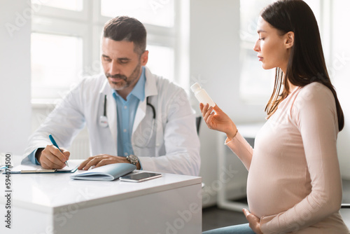 Male doctor rescribing drugs for young pregnant lady  woman holding bottle with pills  therapist explaining prescription