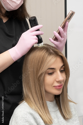 Consultation with a trichologist. The doctor examines a macro video from a trichoscope on the screen of a mobile phone. examination of the scalp and hair follicles of a caucasian female patient 