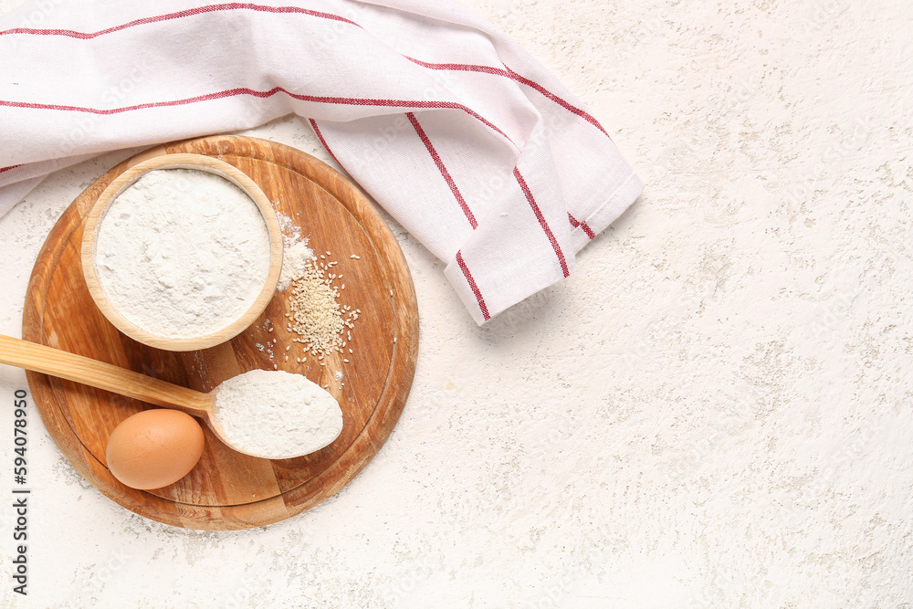 Board with bowl of wheat flour, sesame seeds, spoon and egg on white grunge table Board with bowl of wheat flour, sesame seeds, spoon and egg on white grunge table