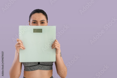 Sporty young woman with scales on lilac background