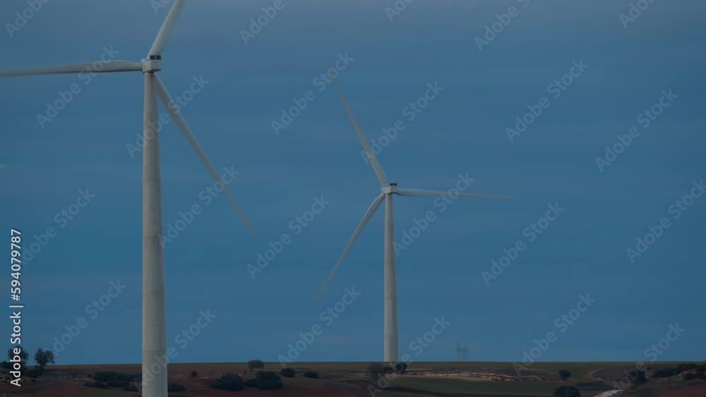 Two windmills stand tall in a field during evening hours, with a beautiful blue sky as the backdrop Two windmills stand tall in a field during evening hours, with a beautiful blue sky as the backdrop