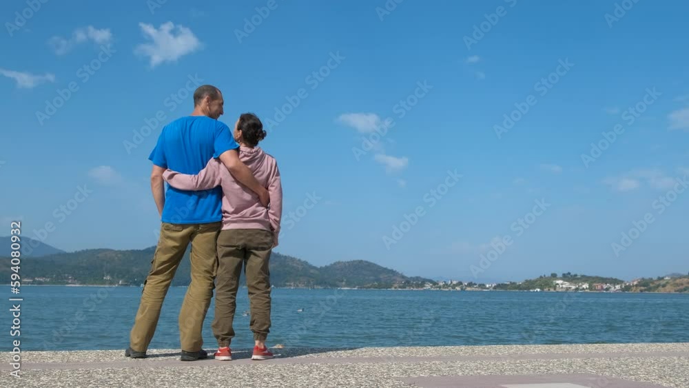 Family couple backs enjoy exotic coastline. A view of family couple stay on the beach and enjoy the sea scape in the day light during summer vacation. Family couple backs enjoy exotic coastline. A view of family couple stay on the beach and enjoy the sea scape in the day light during summer vacation.