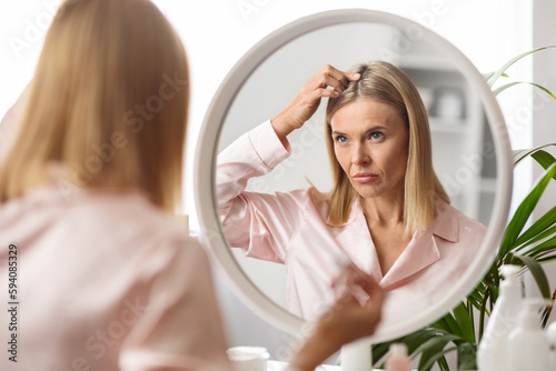 Upset Middle Aged Lady Looking In Mirror At Her Hair Roots