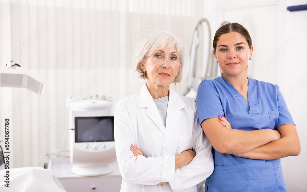 Obraz premium Two smiling woman doctors posing against background of cosmetology devices in aesthetic clinic