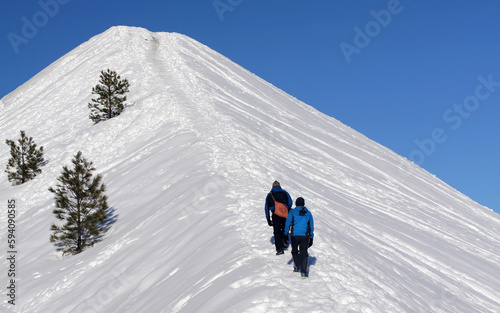 Two people exploring the Northwest Wilderness walking up a steep snow covered hill.