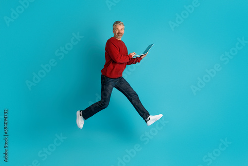 Excited middle aged man digital nomad jumping with laptop