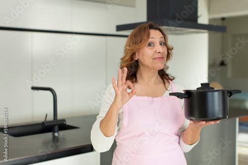 middle age pretty woman feeling happy, showing approval with okay gesture. cooking at home concept
