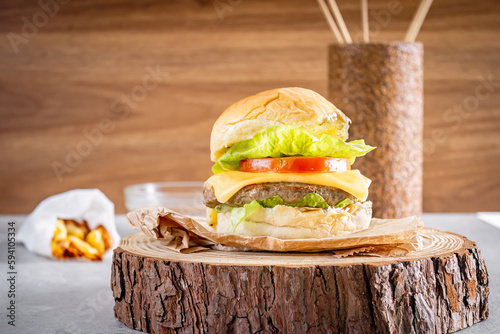 Delicious hamburger with cheddar cheese over wooden log and wooden background. Fries on the side. photo