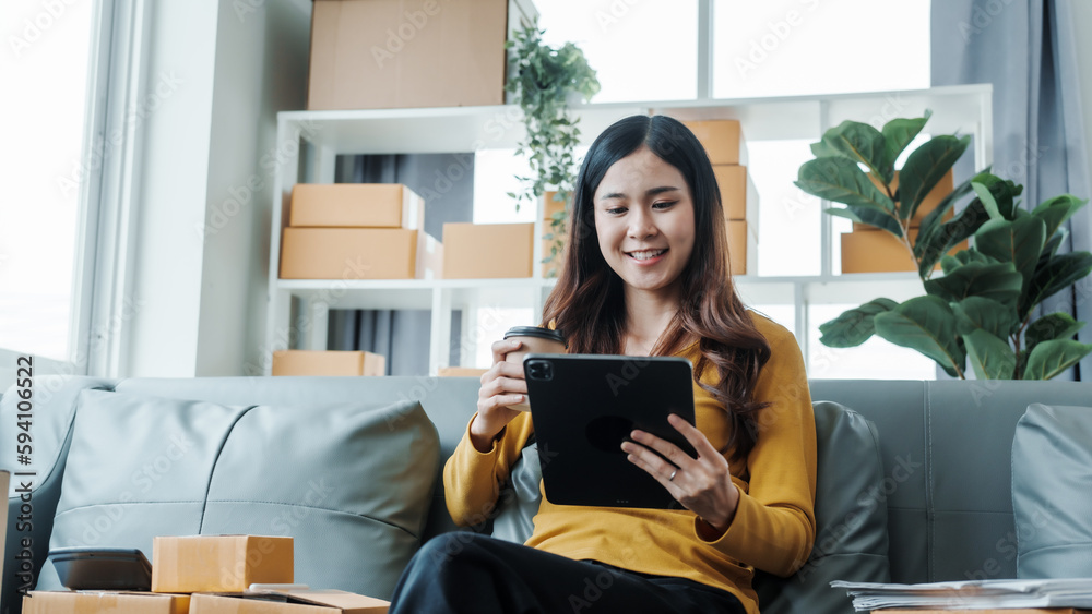Young pretty Asian female influencer small businesses SME owners female entrepreneurs working on receipt box and check online orders, sitting on sofa of home online business. Young pretty Asian female influencer small businesses SME owners female entrepreneurs working on receipt box and check online orders, sitting on sofa of home online business.