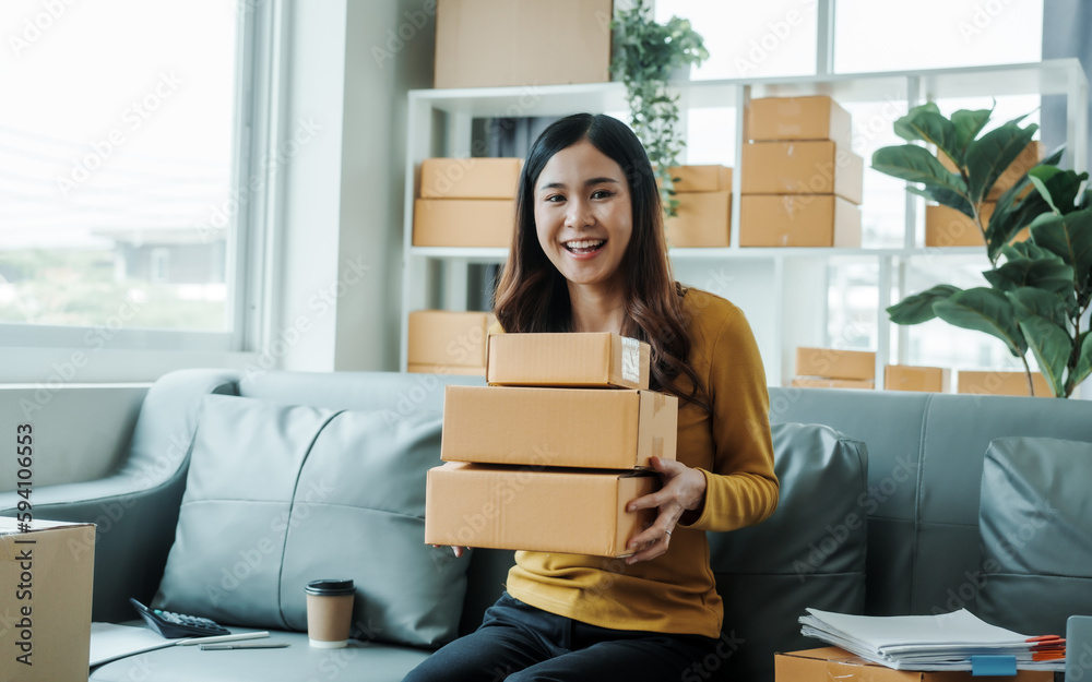 © Phushutter - Young pretty Asian female influencer small businesses SME owners female entrepreneurs working on receipt box and check online orders, sitting on sofa of home online business.