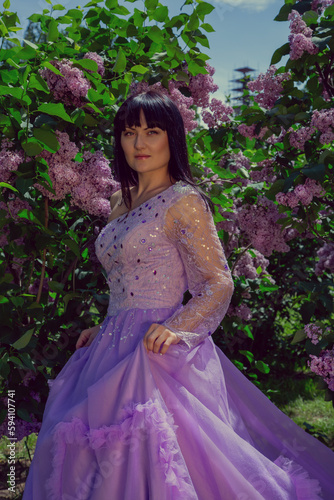 Young brunette woman in a beautiful dress in a garden with blooming purple bushes.