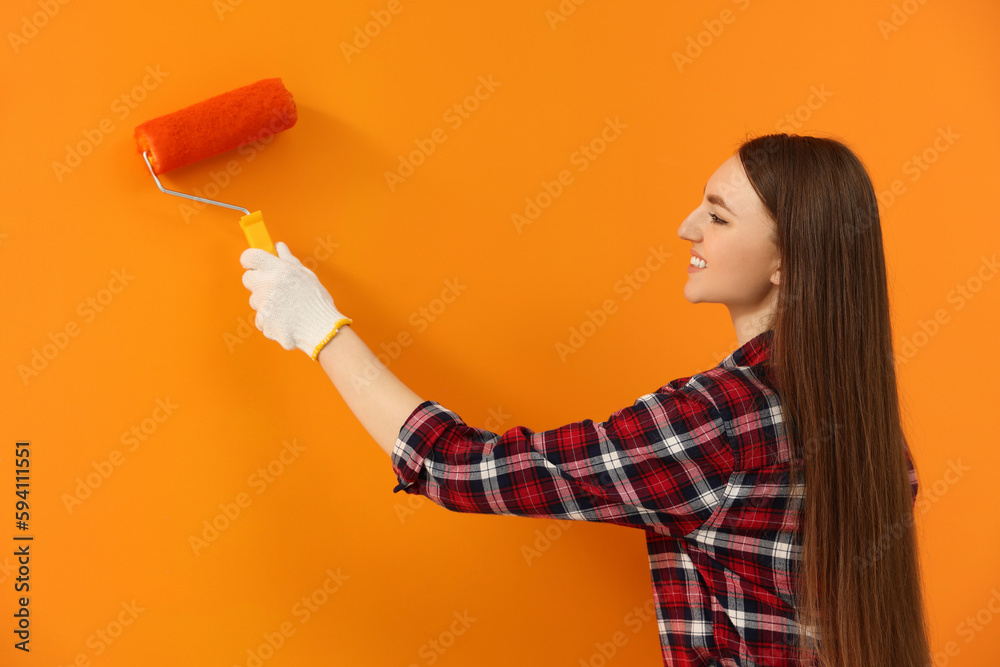 Happy designer painting orange wall with roller Happy designer painting orange wall with roller