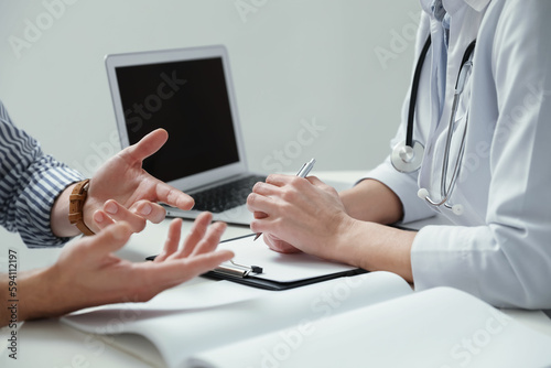 Doctor consulting patient at white table indoors, closeup