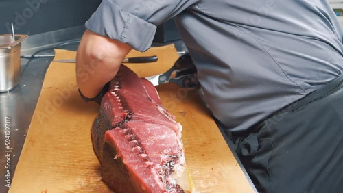Close-up of the process of cutting tuna fish at the market. Male hands in gloves cutting a large fish with a knife.