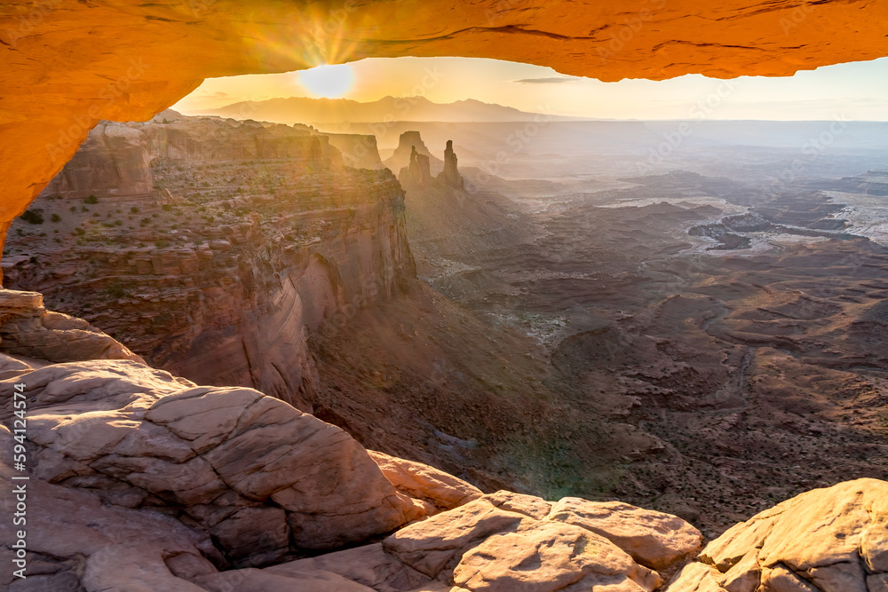 A phenomenal landscape scene of a rock opening with view of distance mountains and cliffs back illuminated by the rising sun, Mesa Arch at sunrise, Island In the Sky, Canyonlands, Utah